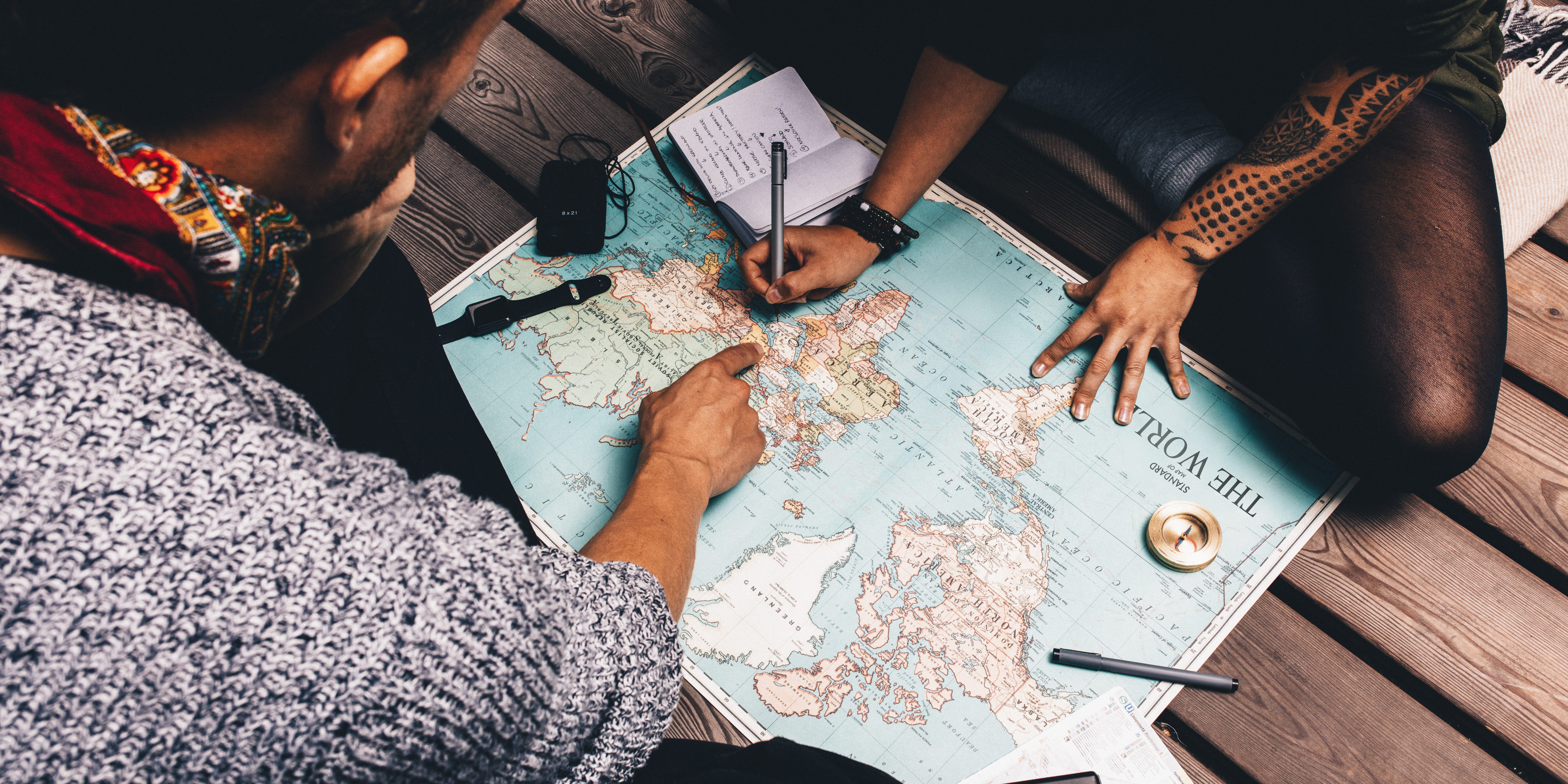 Couple planning vacation using a world map. Man pointing at the map while the woman is making notes in diary.