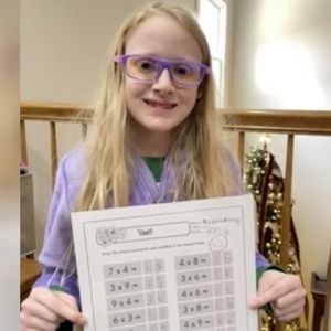 Girl holding a multiplication test with a 100% score.