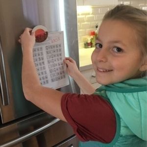 Girl putting a multiplication test with a 100% score on the refrigerator.