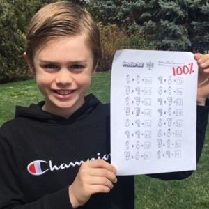 Boy providing a Times Tales review by holding up a multiplication test with a 100% score.