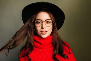 Portrait of dark-haired Caucasian woman in red sweater and wide-brimmed hat on gray background