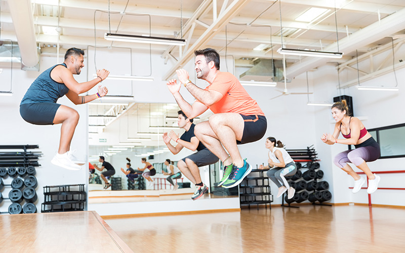 Full length of male trainer doing tuck jumps with clients in health club